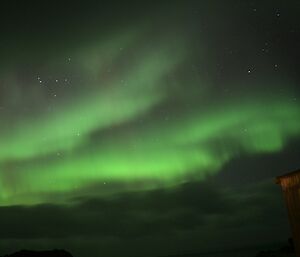 A beautiful, bright aurora seemingly reaches out to a building at night on Macquarie Island