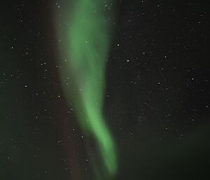 A vertical aurora australis, similar in shape to a cone, hangs in the night sky