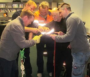 Five expeditioners in a tight circle peer intently at a rope end.