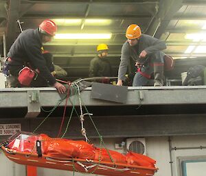 Two expeditioners lower stretcher over vertical drop