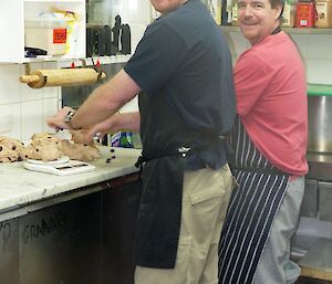 Two men working in the kitchen look over their shoulders to the photographer