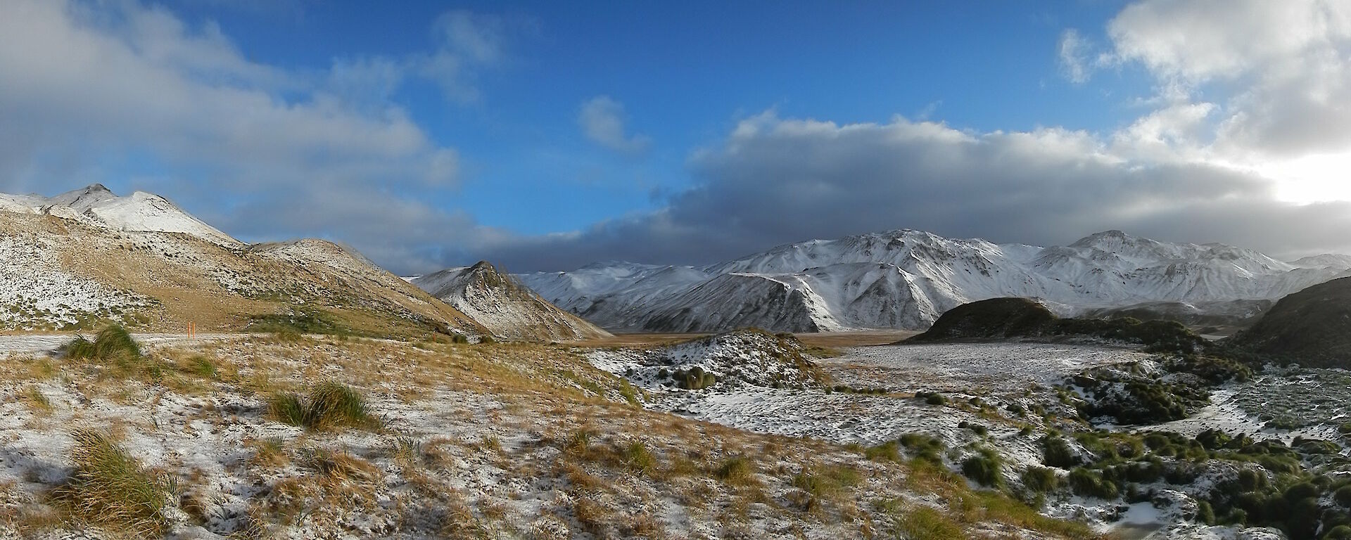 The grassy slopes of Green Gorge — a panoramic landscape image that also shows snow-capped mountains