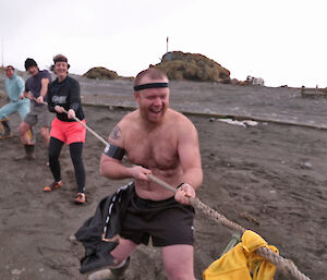 Greg in tug of war, wearing no shirt and a bandana, laughs