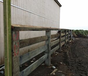 Fence and railing next to a building with dirt to the right, covered in vehicle tracks