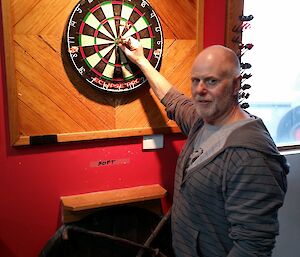 Graeme stands before a dartboard where he has hit a bullseye
