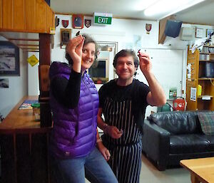An expeditioner and chef pose with darts pointed at camera