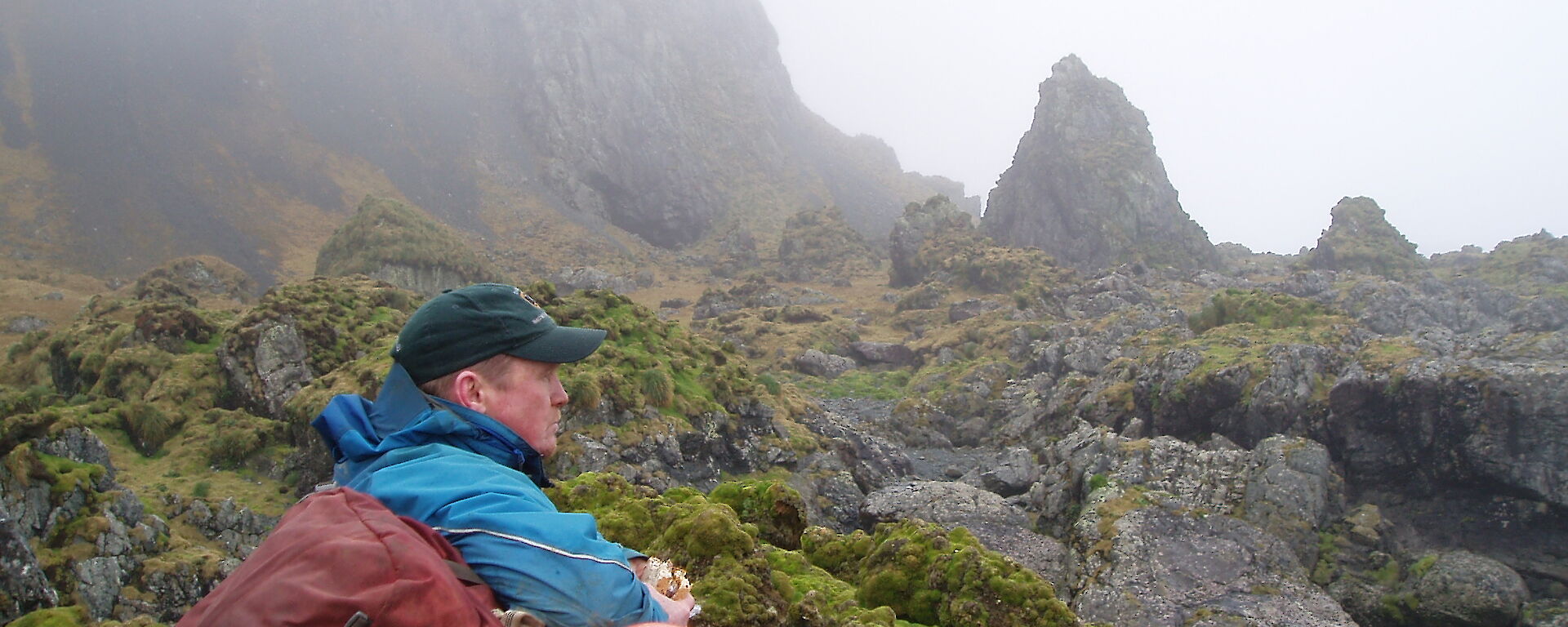 Ranger Chris sits amongst the mossy rocks of Macquarie Island looking reflective