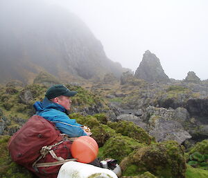 Ranger Chris sits amongst the mossy rocks of Macquarie Island looking reflective