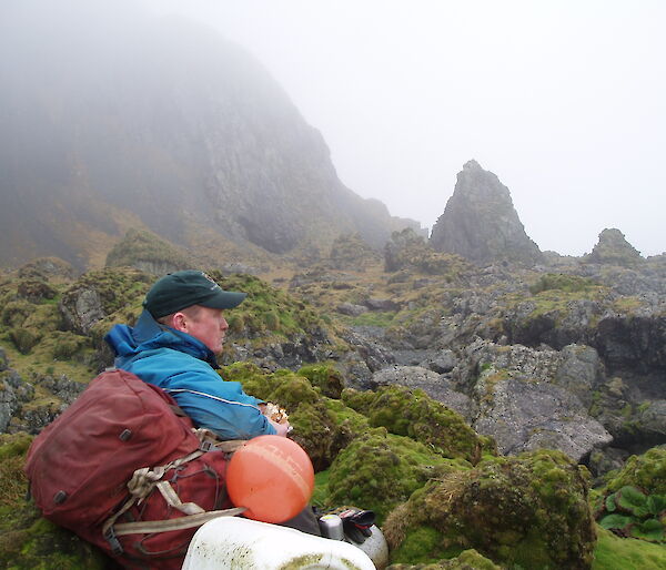 Ranger Chris sits amongst the mossy rocks of Macquarie Island looking reflective