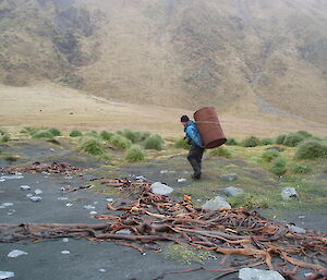 Chris transports a rusty fuel drum to the debris cache