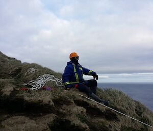 An expeditioner sits on a hill enjoying the view over the water