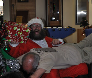 A male expeditioner lies across Santa’s knees eliciting a big smile