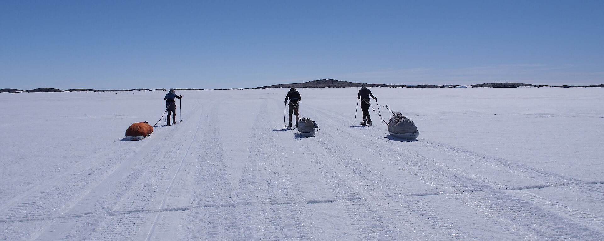 Three expeditioners pulling sleds of gear on the sea ice across to an island