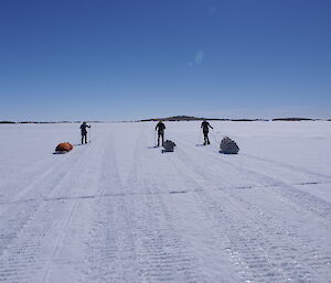 Three expeditioners pulling sleds of gear on the sea ice across to an island