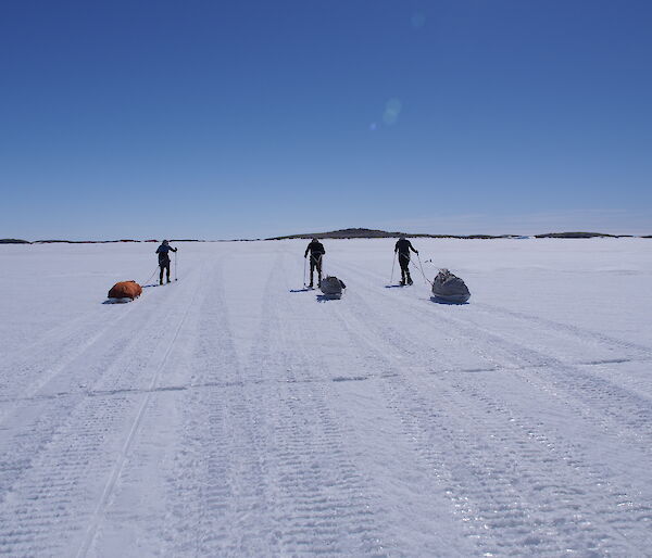 Three expeditioners pulling sleds of gear on the sea ice across to an island