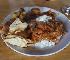 On a plate curry, rice, papadams, rotis and yoghurt