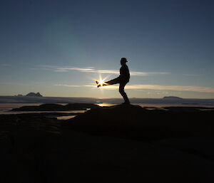 Biologist with outstretched leg at night with the sun setting and appearing as if it is on top of her foot like she is playing with a hacky sack