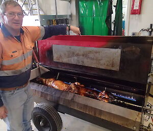 An expeditioner alongside a lamb on a spit