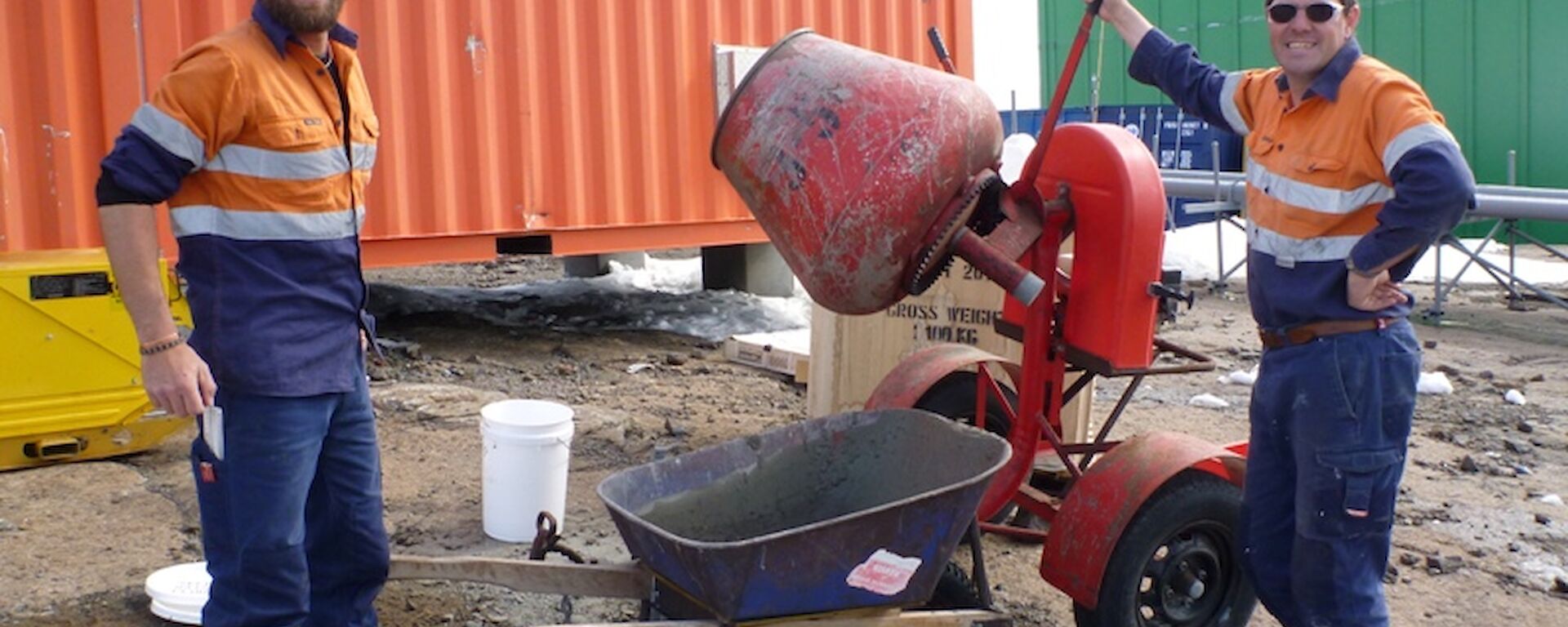 Two expeditioners standing beside a cement mixer and wheel barrow