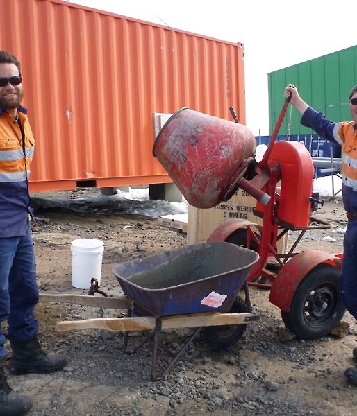 Two expeditioners standing beside a cement mixer and wheel barrow