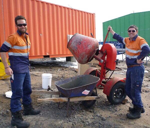 Two expeditioners standing beside a cement mixer and wheel barrow