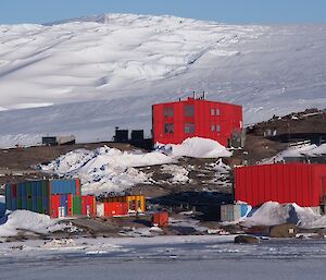 The buildings of Mawson station with the Antarctic plateau rising steeply behind the station