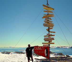 An expeditioner leans on the tall Casey signpost