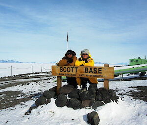 Two expeditioners lean over a sign for Scott Base