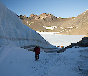 An expeditioner poses in the shadow of a high, icy wall created by a wind scour