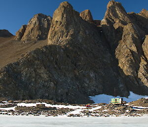 Rumdoodle Hut is dwarfed by rocky peaks just behind and you can see snow in the foreground