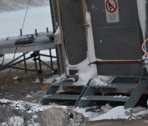 Eleaphant seal dusted with snow photographed near metal steps leading to a small building at Mawson station