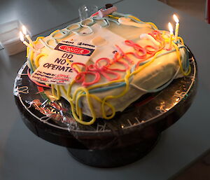 Electrician themed birthday cake featuring warning sticker and words written out in electrical cords made of icing