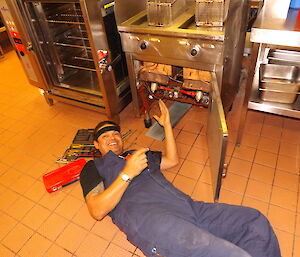 An expeditioner does work lying down on his back in the kitchen at one of the deep fryers