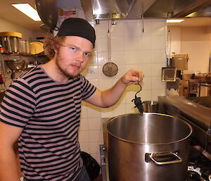 Keldyn Francis in kitchen holding a rubber rat over a large pot on the stove