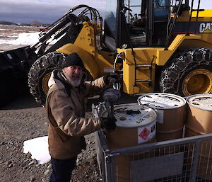 Geoff Brealey at work outside near storage drums with excavator in background