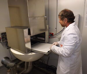 ARPANSA filter change by Craig Heyhow in a lab wearing a white coat posing in front of a metal box