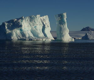 A large iceberg on left with a tall cylindrical iceberg to its right