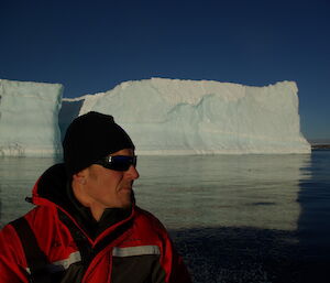 Justin C viewed from chest up in an inflatable rubber boat with a very large iceberg in background