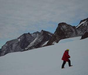 An expeditioner walks up a snowy hill at the David Range under an overcast, grey sky