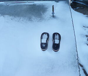 Boots in frozen upside down in concrete and surrounded by snow so you can only see the bottoms of the shoes