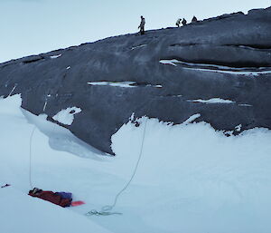 Mawson SAR exercise — a small rocky cliff with expeditioners at the top lowering a rope to a mock fall victim at the bottom on a rescue board