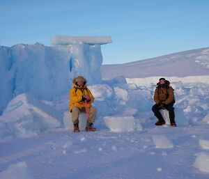 Two expeditioners sit in front of a collapsed ice cliff