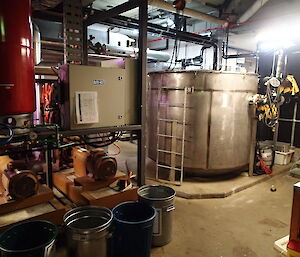 Plant room full of equipment with a large metal cylinder waste water vat in the middle