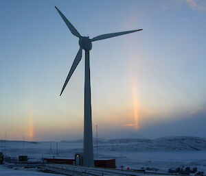 Solar pillar — a column of sunlight beams down from the sky behind the Mawson wind turbine