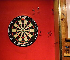 Dart board with darts embedded in the wall around it