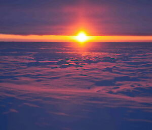 Plateau sunset exploding through brilliantly purple clouds above and ice below