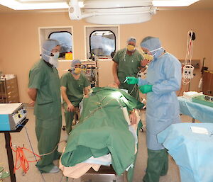 Expeditioners in scrubs stand around a mock patient in an operating theatre