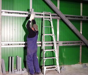 Starting work on climbing wall, an expeditioner in blue overalls lifts a metal brace in place