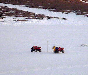 Measuring sea ice, a man kneels behind two quad bikes