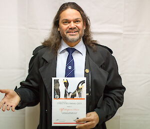 Cliff Simpson-Davis dressed in a suit and tie holding his Director’s Award certificate